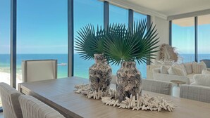 A dining table with two vases and a palm plant, overlooking a beach view.