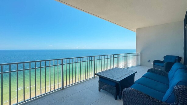 A balcony with a view of the ocean, a table, and two blue sofas.