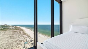 A hotel room with a large window offering a view of a beach and ocean.