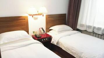 Habitación de hotel con dos camas individuales, cabecero de madera, mesita de noche con lámpara y ventana con cortinas.