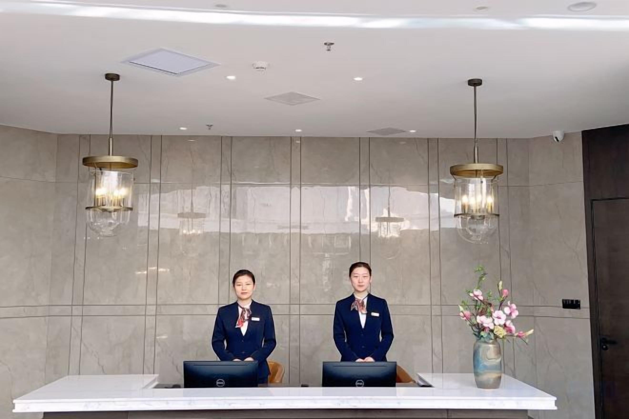Mostrador de recepción con dos empleados, un florero y lámparas colgantes modernas.
