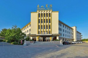 A multi-story hotel with a central entrance, a parking lot, and a clear sky. - Dongshan Hotel (Anshan)