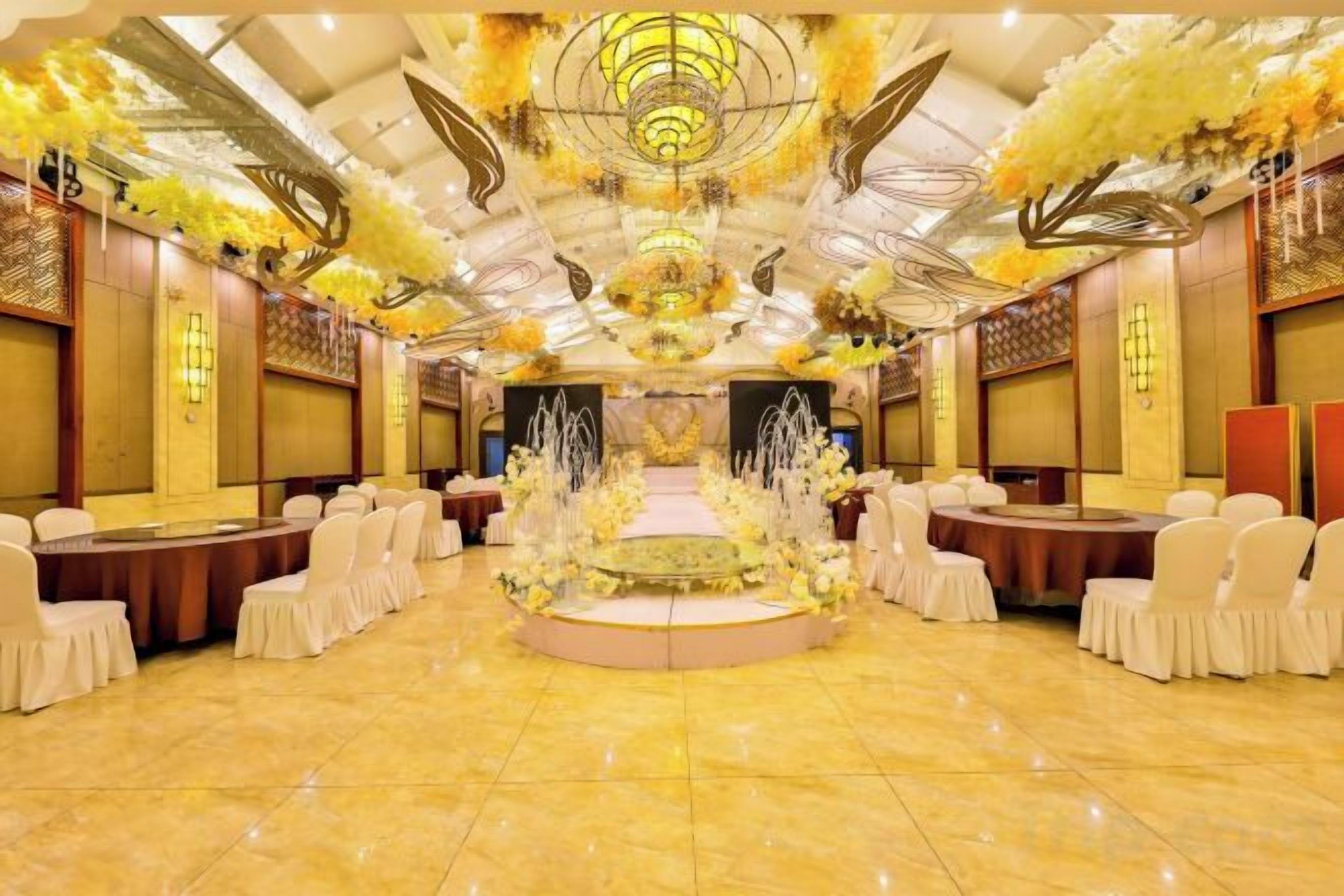 A banquet hall with a central stage, round tables, and chairs arranged for an event.