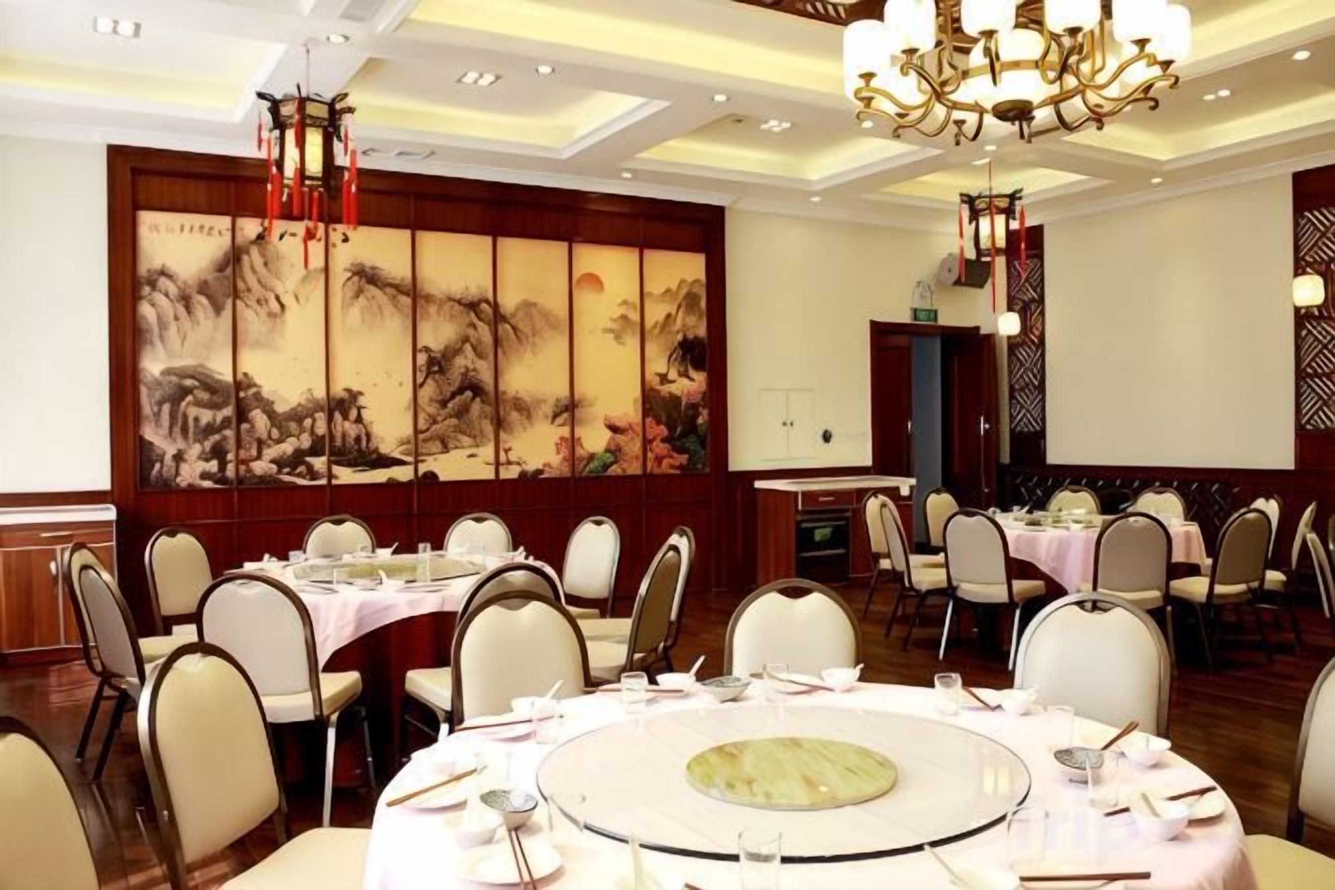 A banquet hall with round tables, chairs, and a traditional Chinese painting on the wall.