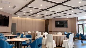 Un salón de conferencias con mesas y sillas, una pantalla grande y vistas al exterior.