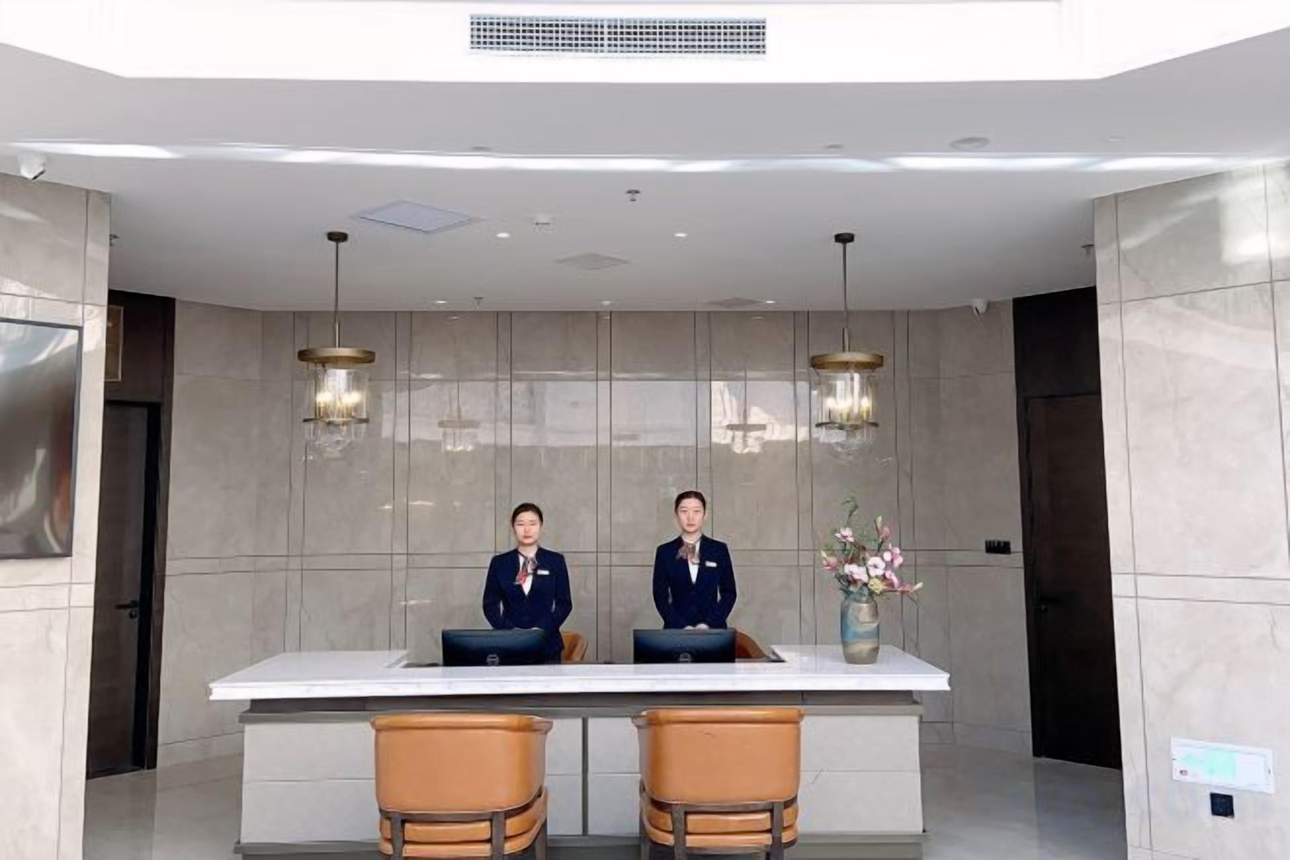 A reception desk with two uniformed staff, a large white counter, and two brown chairs.