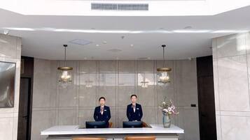 A reception desk with two uniformed staff, a large white counter, and two brown chairs.