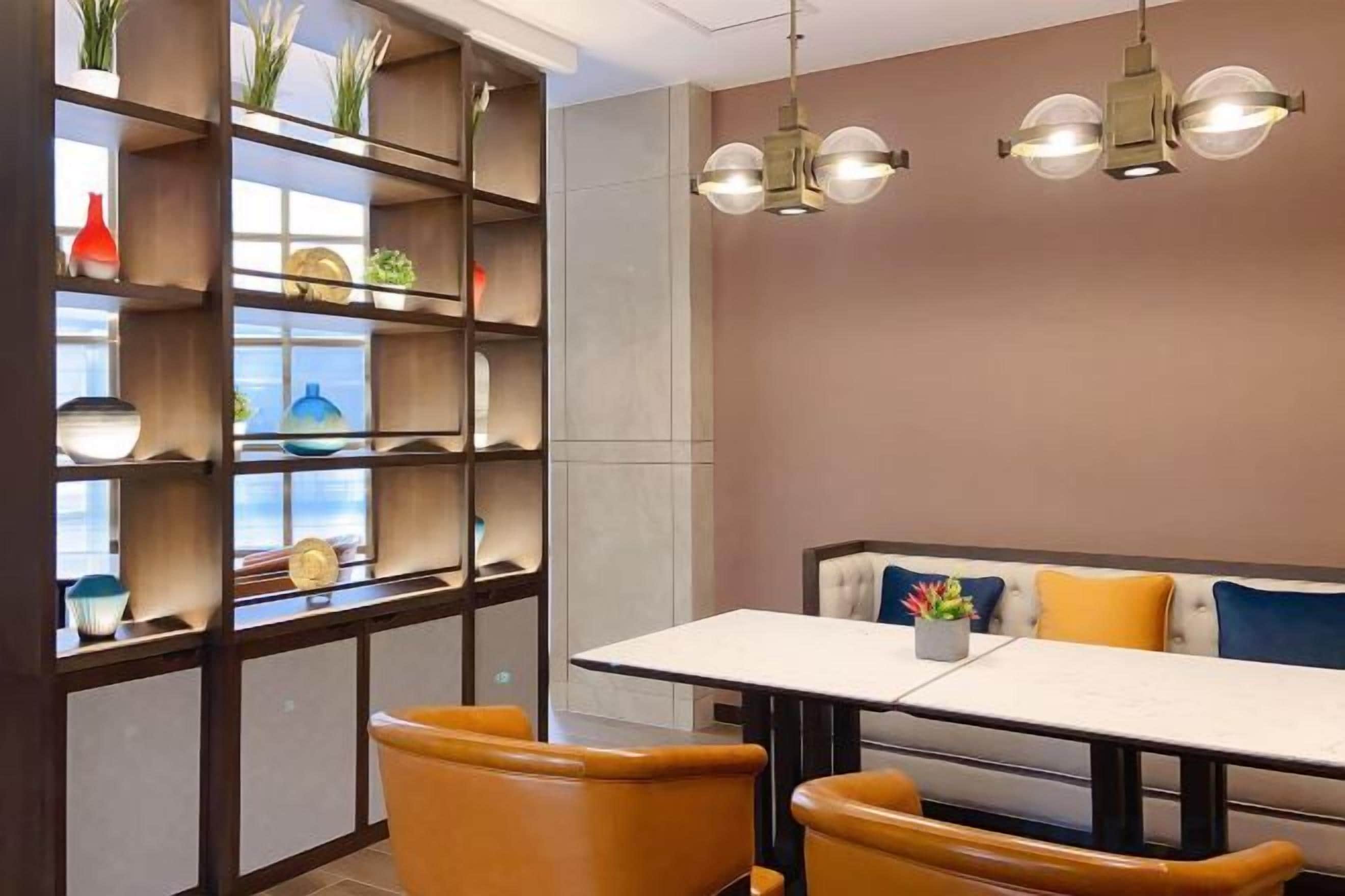 A dining area with a table and chairs, a bookshelf with decorative items, and pendant lighting.