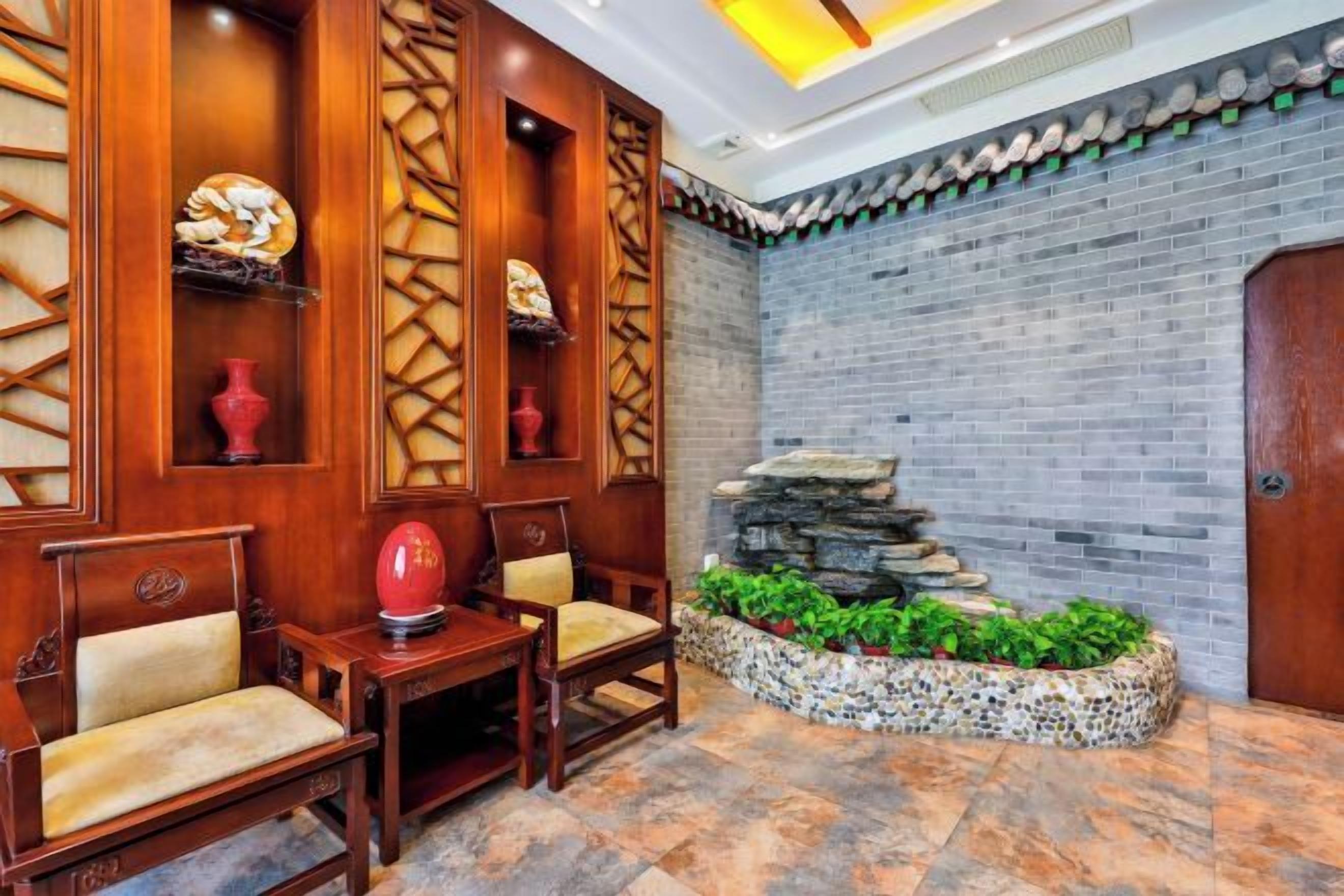 A lobby with wooden paneling, a stone water feature, and a seating area with chairs and a table.