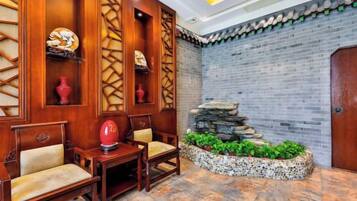 A lobby with wooden paneling, a stone water feature, and a seating area with chairs and a table.
