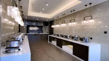 A modern kitchen with a long counter, multiple food dispensers, and pendant lighting.