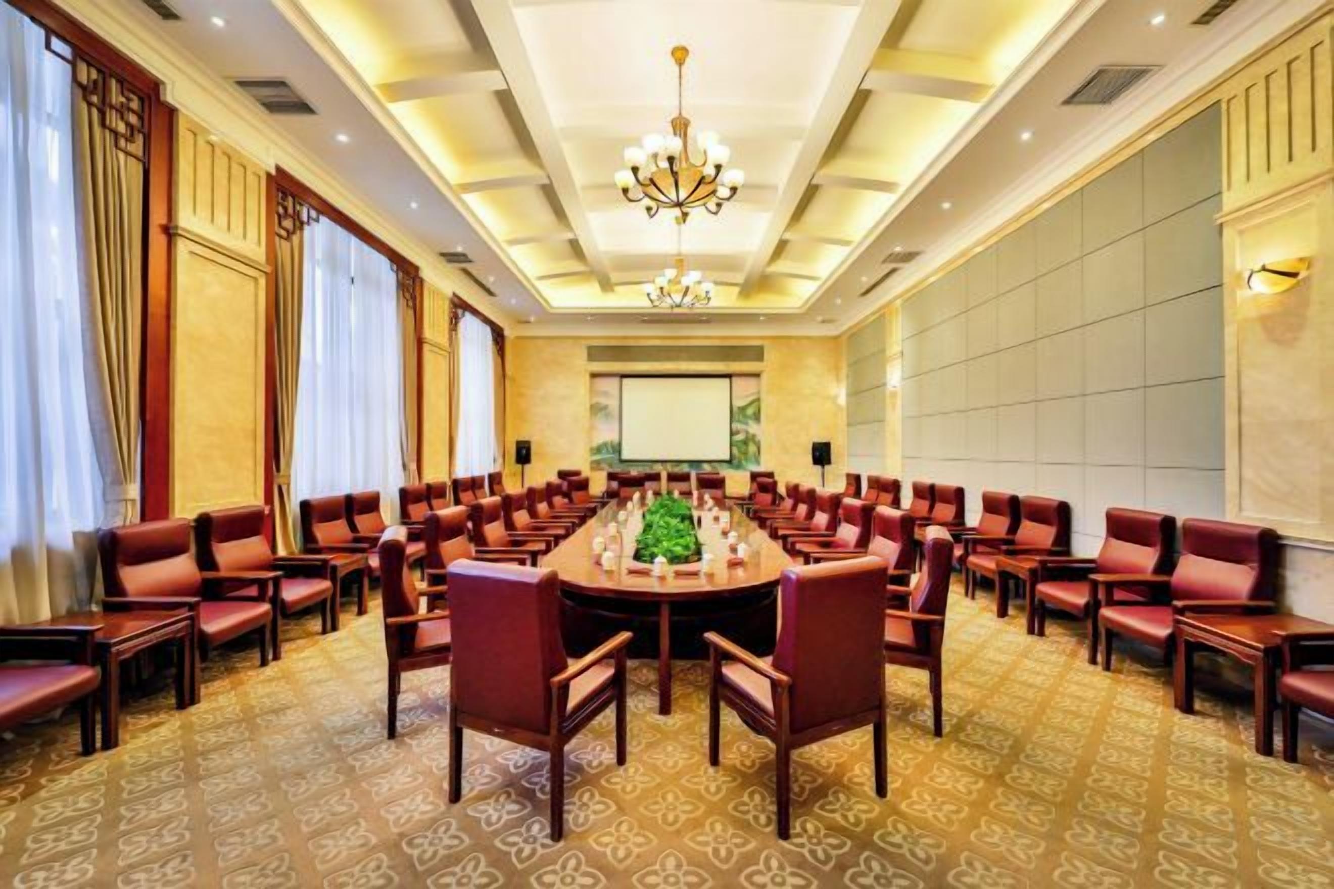 A conference room with a large oval table surrounded by chairs, a projector screen, and a chandelier.