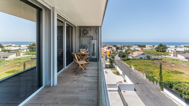 Een balkon met een tafel en stoelen, met uitzicht op een woonwijk en de zee.