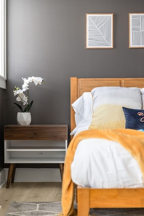 Un dormitorio con cama, mesita de noche, cómoda y dos obras de arte enmarcadas en la pared.