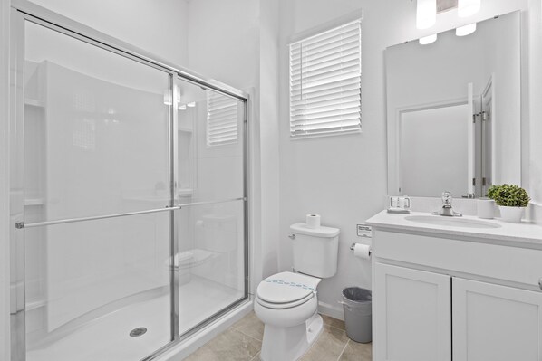 Une salle de bain moderne avec une douche à l’italienne en verre, des toilettes, un lavabo avec un miroir et une plante en pot.