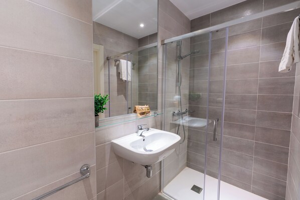 Un baño moderno con cabina de ducha de vidrio, un lavabo blanco y un estante de vidrio.