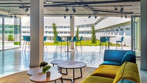 A modern indoor space with seating, tables, and a view of buildings outside. - STUDENT EXPERIENCE MADRID POZUELO (Pozuelo de Alarcon)