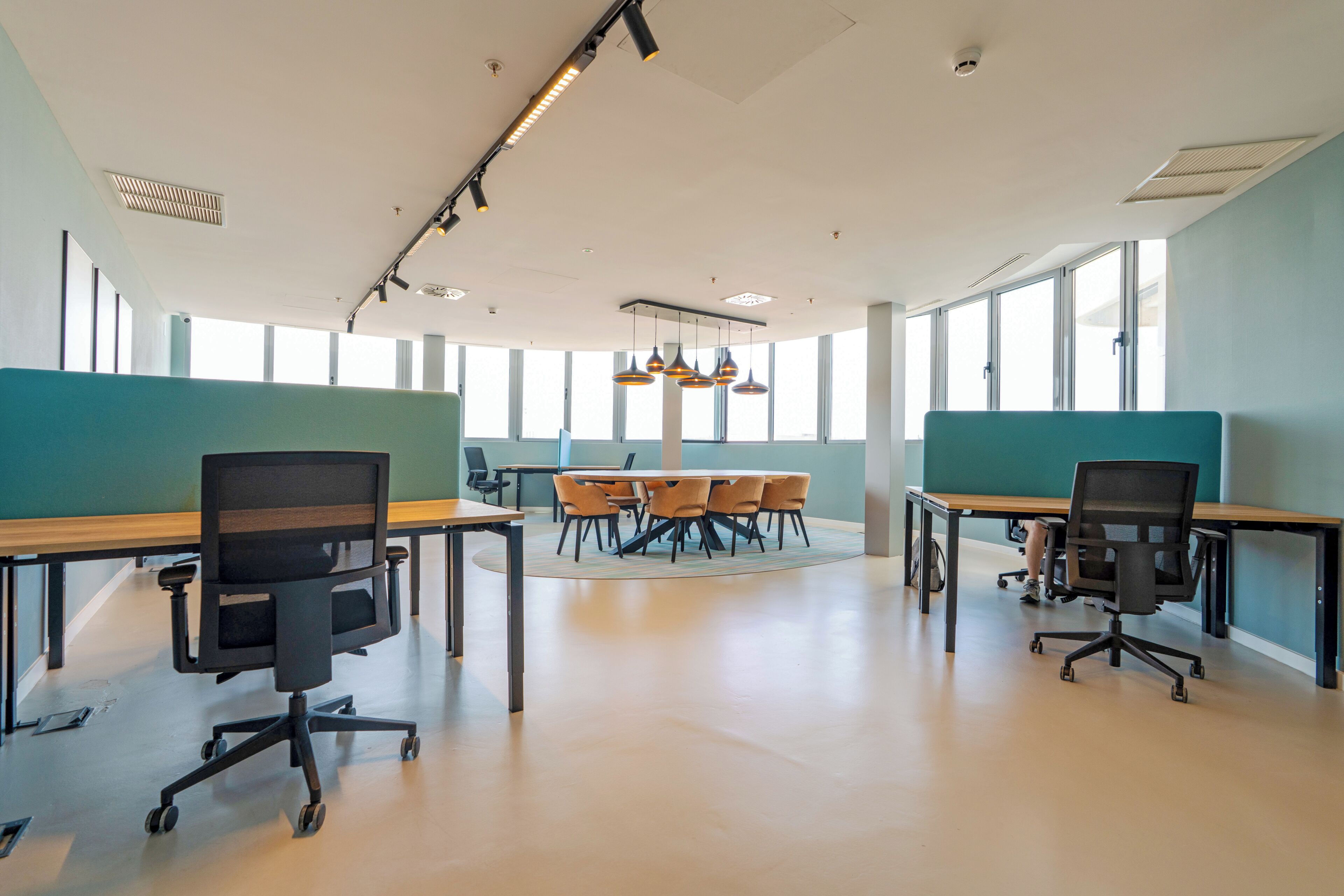 An office space with a round table, multiple chairs, and individual workstations.