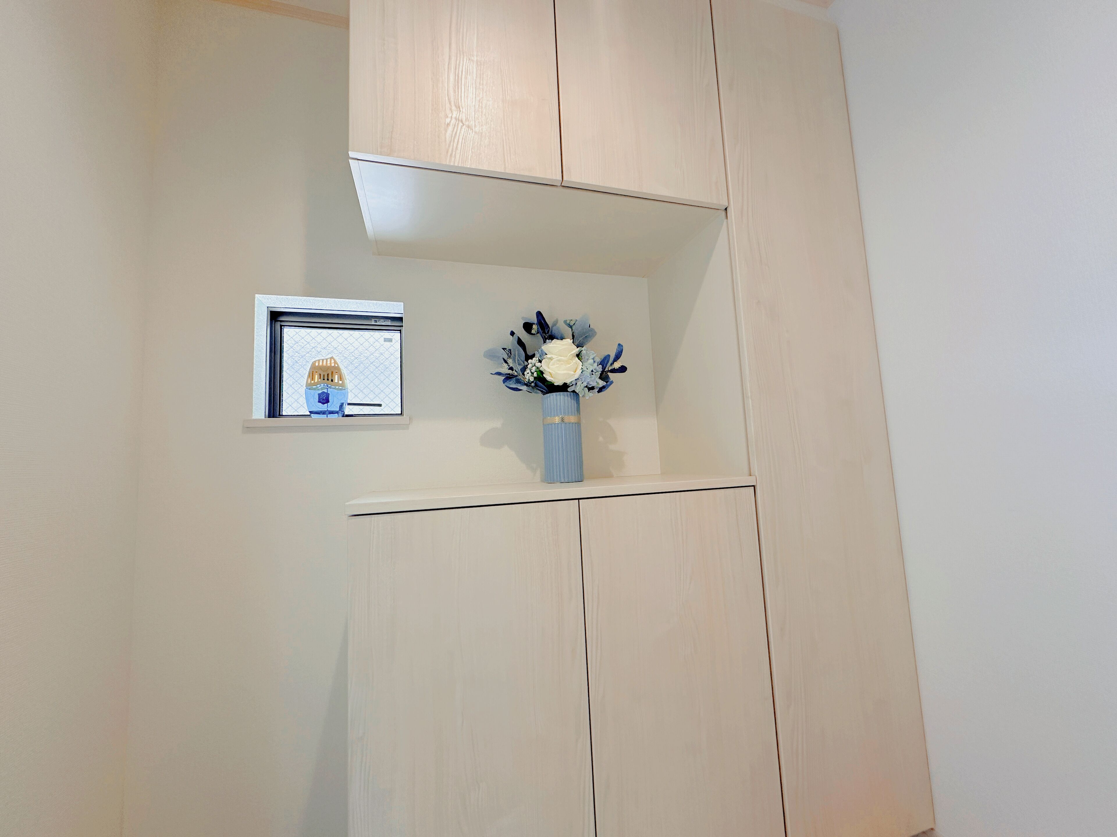 A room with a light-colored wardrobe, a small framed picture on the wall, and a vase with flowers.