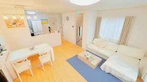 Un salon moderne avec un canapé blanc, une petite table et un fauteuil. Un tapis bleu recouvre le sol, et un miroir est accroché au mur.