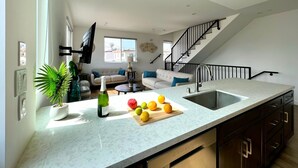 A modern kitchen with a large island, a dining area with a sofa, and a staircase leading to an upper level. - Truly Special LA Gem private rooftop deck VIEWS (Los Angeles)