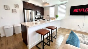 A modern kitchen with stainless steel appliances, a central island with stools, and a flat-screen TV mounted on the wall. - Truly Special LA Gem private rooftop deck VIEWS (Los Angeles)