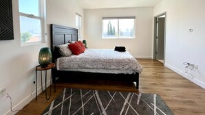 A modern bedroom with a large bed, two windows, a wooden floor, and a visible door. - Truly Special LA Gem private rooftop deck VIEWS (Los Angeles)