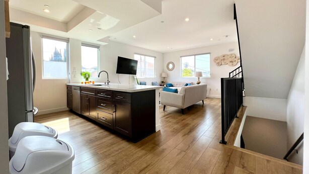 A modern kitchen with a central island, a dining area with a sofa, and a staircase leading to an upper level. - Truly Special LA Gem private rooftop deck VIEWS (Los Angeles)