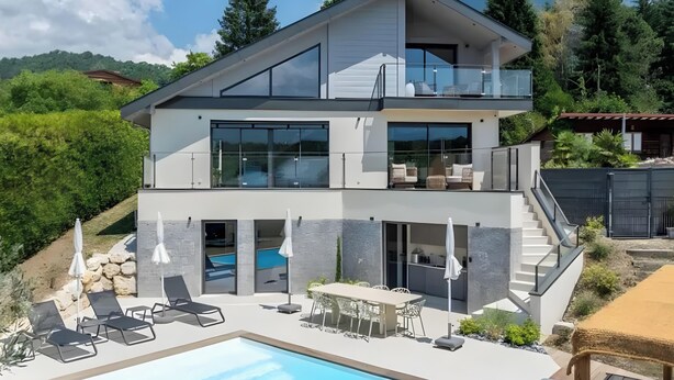 Une maison moderne à deux étages dotée d’une piscine, d’un espace salon extérieur et offrant une vue sur les montagnes.