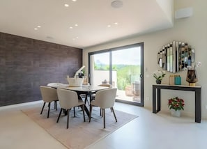 Un comedor moderno con un ventanal de vidrio que da a un balcón, una pared oscura y una consola decorada con adornos.
