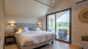 Une chambre à coucher avec un lit, des lampes de chevet, une table de nuit, une grande fenêtre et une vue sur l’extérieur.