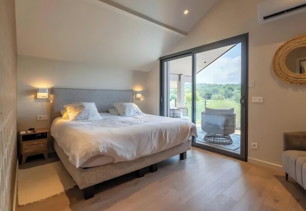 Une chambre à coucher avec un lit, des lampes de chevet, une table de nuit, une grande fenêtre et une vue sur l’extérieur.
