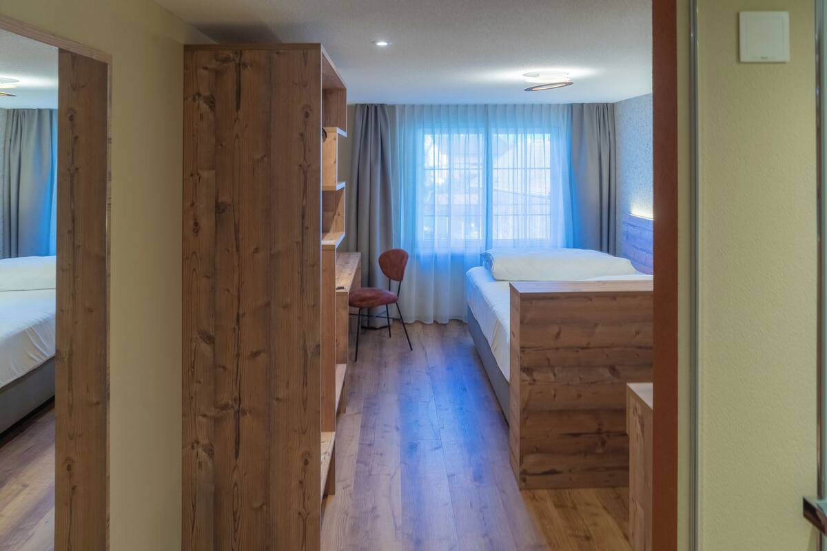 A hotel room with wooden flooring, a bed, a desk, and a chair.