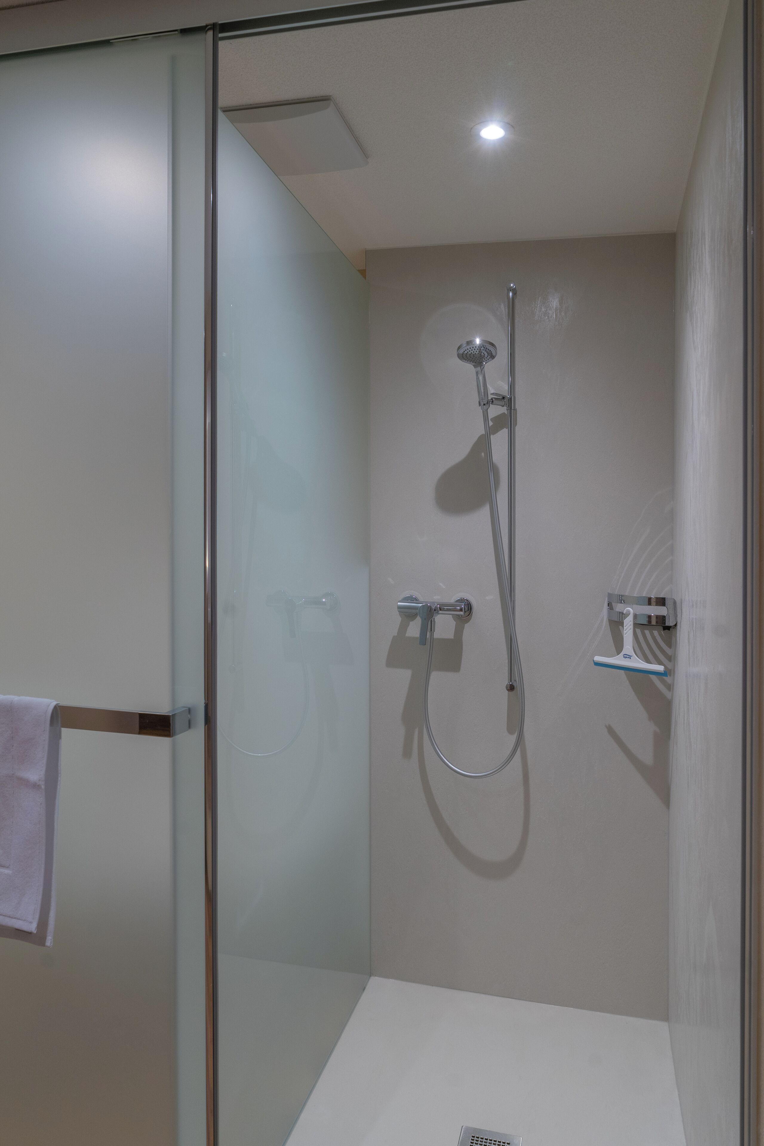 Um chuveiro moderno com porta de vidro, um chuveiro manual e uma torneira fixada na parede.