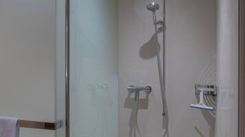 Um chuveiro moderno com porta de vidro, um chuveiro manual e uma torneira fixada na parede.