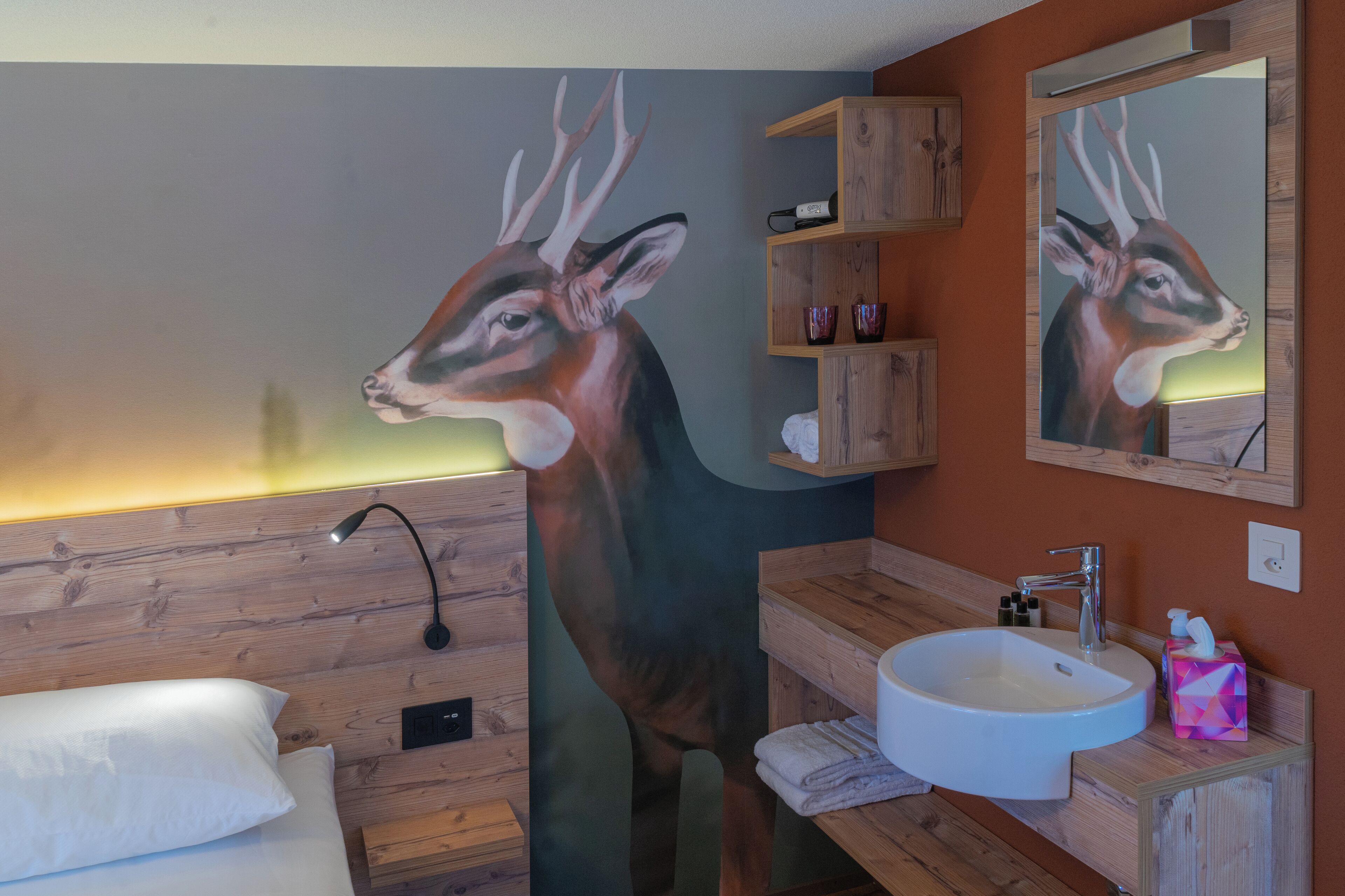 A bathroom with a large deer mural, wooden shelves, a sink, and a mirror.