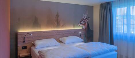 A modern bedroom with a large bed, a headboard with a wall mural, a bedside table, and a window with curtains.