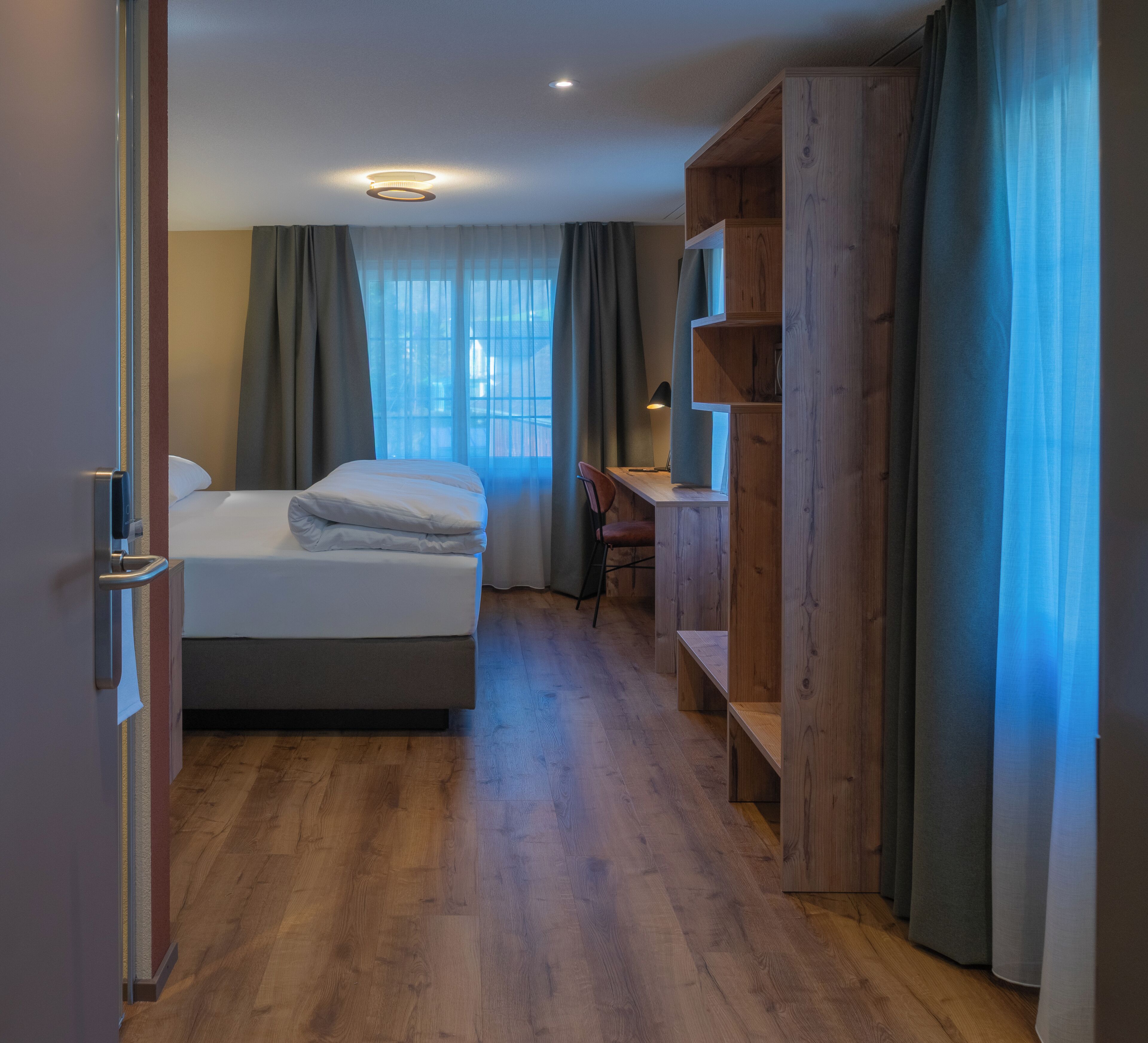 Une chambre d’hôtel avec un lit, un bureau et une étagère en bois.