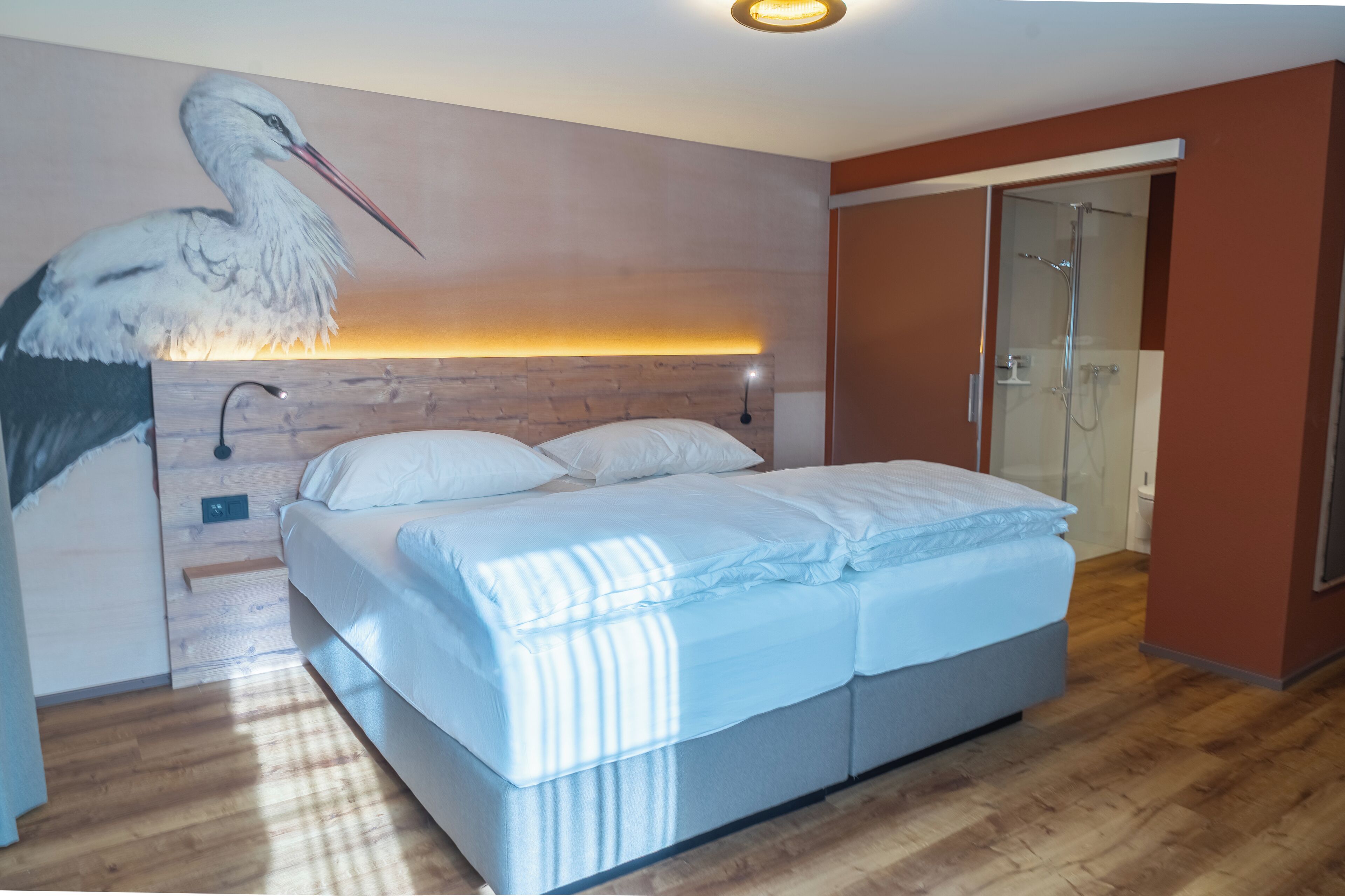 A bedroom with a large bed, a wooden headboard, a wall-mounted light, and a glass shower door.