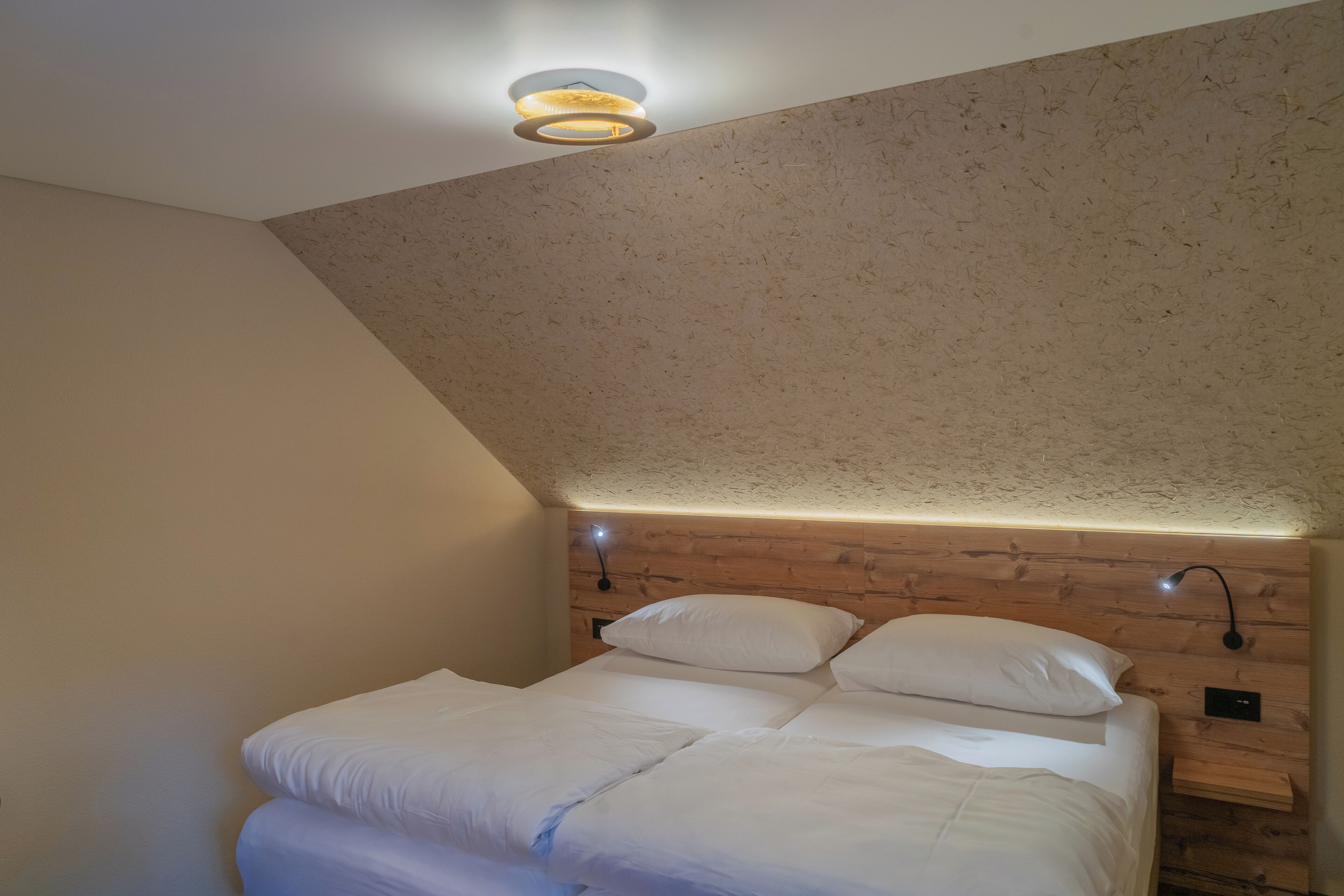A bedroom with a sloped ceiling, wooden headboard, two bedside tables with lamps, and a bed with white bedding.