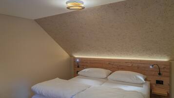 A bedroom with a sloped ceiling, wooden headboard, two bedside tables with lamps, and a bed with white bedding.