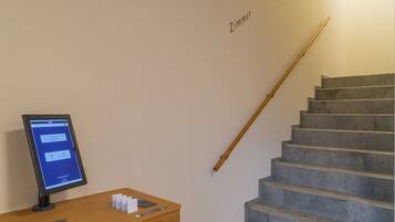 A staircase with a wooden handrail and a digital kiosk on a wooden desk.