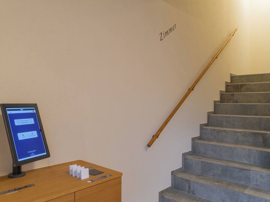 A staircase with a wooden handrail and a digital kiosk on a wooden desk.