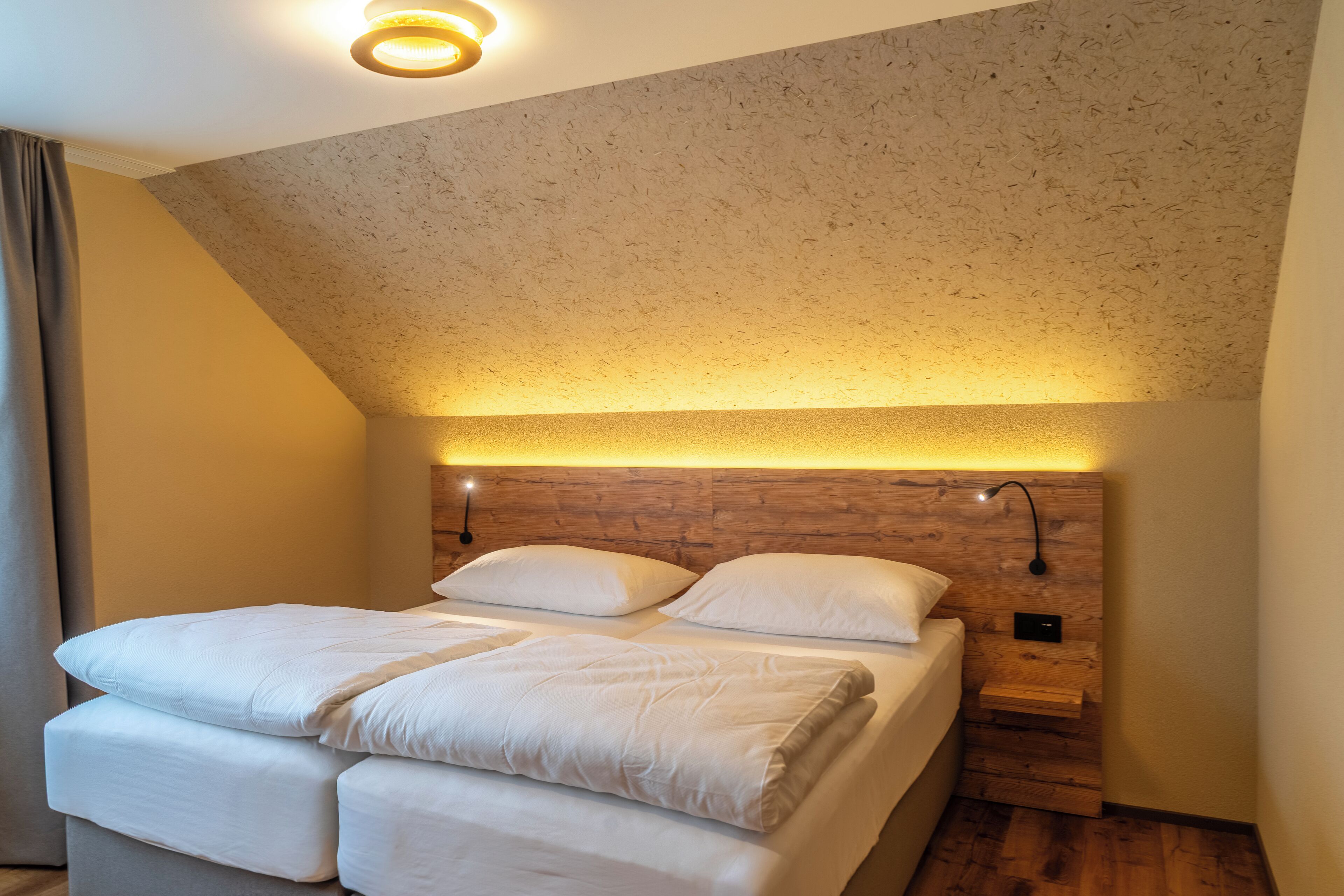 Un dormitorio con cabecera de madera, una cama con ropa de cama blanca y una mesita de noche con lámpara.