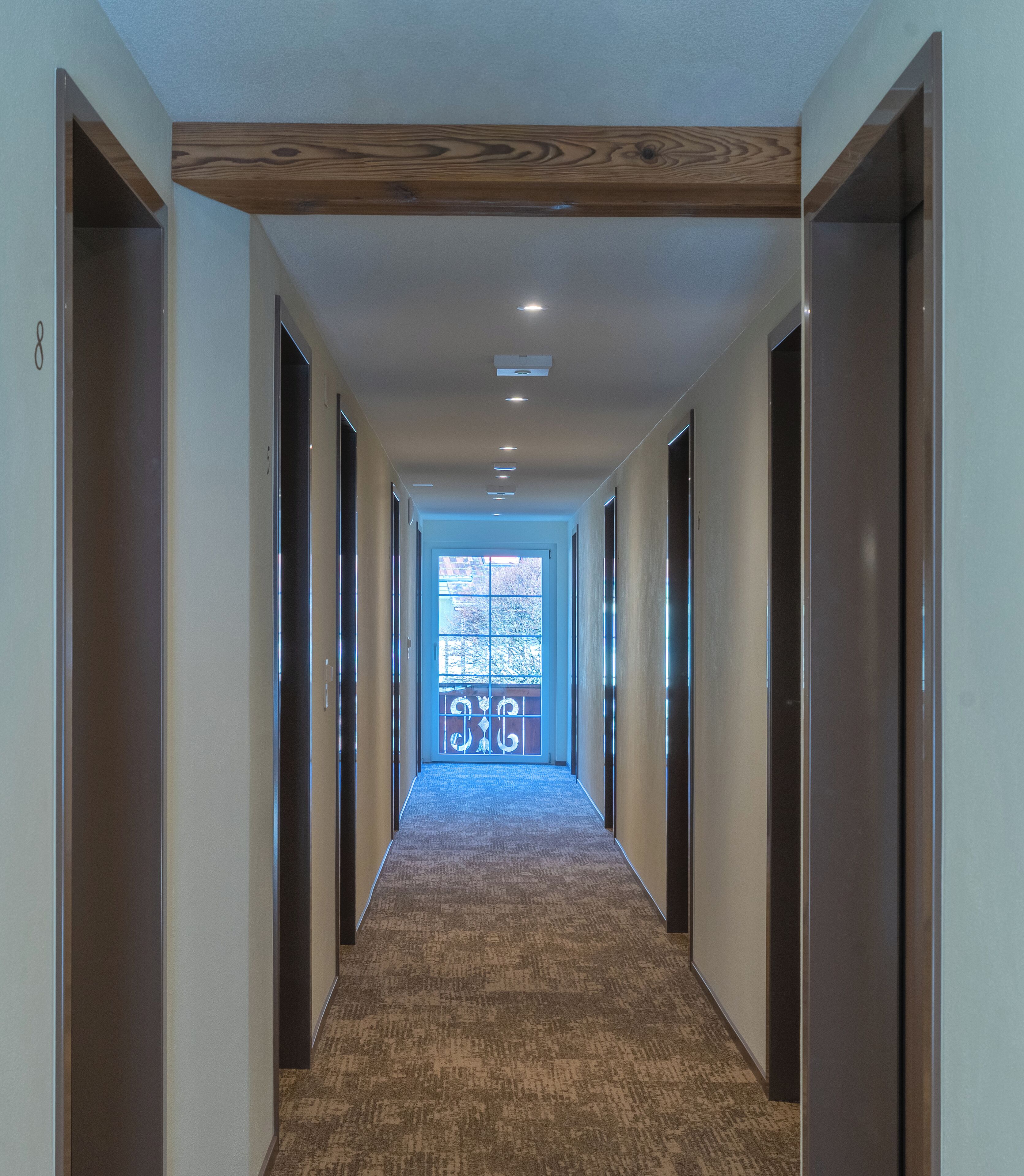 A hallway with a carpeted floor, wooden ceiling beams, and doors on both sides.