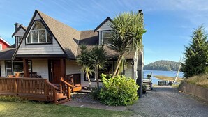 Une maison à deux étages avec un porche à l’avant, une terrasse en bois et une vue sur un lac.