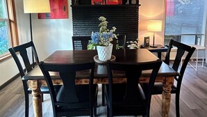 Un coin repas avec une table ronde, des chaises noires, un vase de fleurs, un tableau abstrait rouge et une cheminée en briques noires.