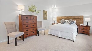 Une chambre à coucher comprenant un lit, deux chaises, une commode, une table de chevet, une lampe et un luminaire fixé au mur.