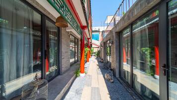 Une ruelle étroite bordée d’immeubles à façade vitrée, avec une cage à oiseaux sur la gauche et un pilier rouge au centre.