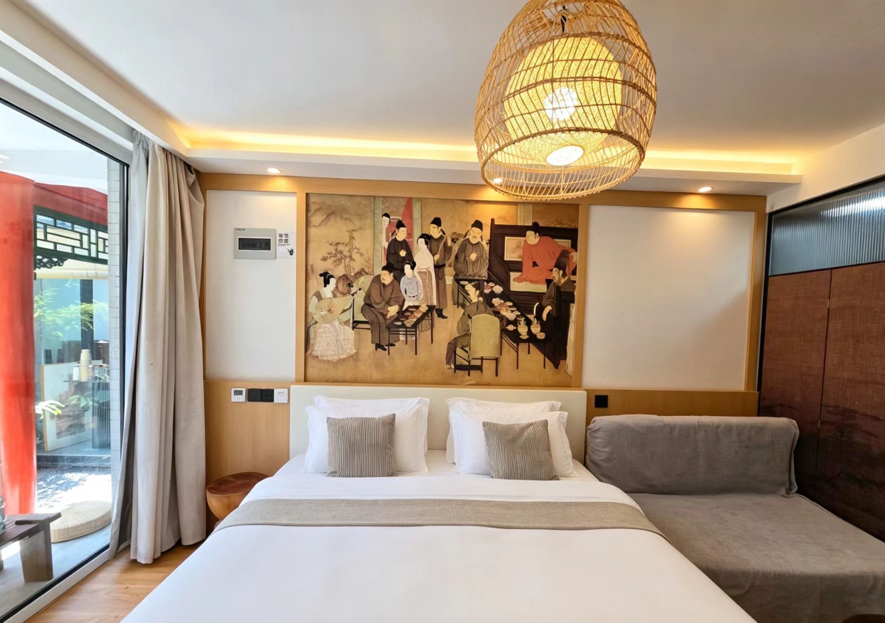 A hotel room with a large bed, a sofa, a traditional painting, and a large window.
